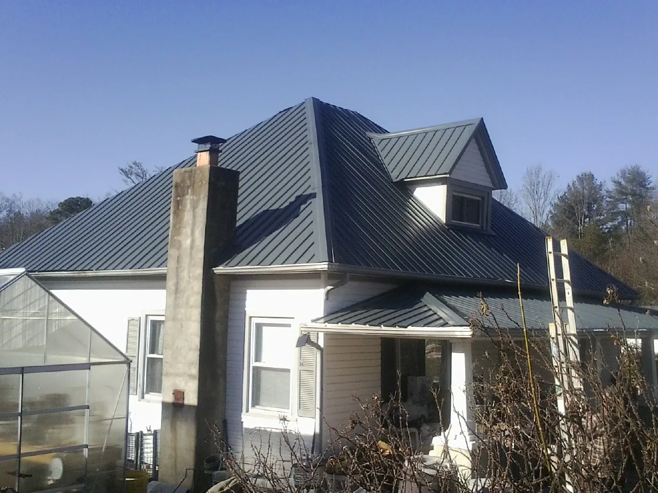 Dark blue standing seam metal roof on a white farmhouse with dormer — Slate & Tile Roof Repair by Roofing Brothers in Live Oak