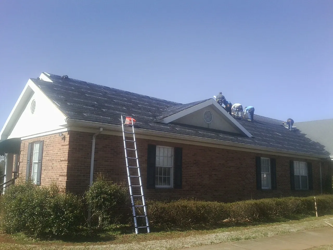 Crew tearing shingles off a brick ranch roof with a ladder set — Metal Roof Repair work by our crew in Live Oak