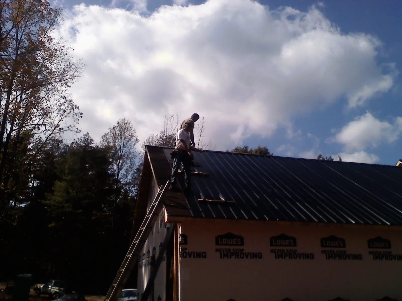 Roofer fastening dark metal panels high against a cloudy sky, from a Roof Inspection job in Live Oak